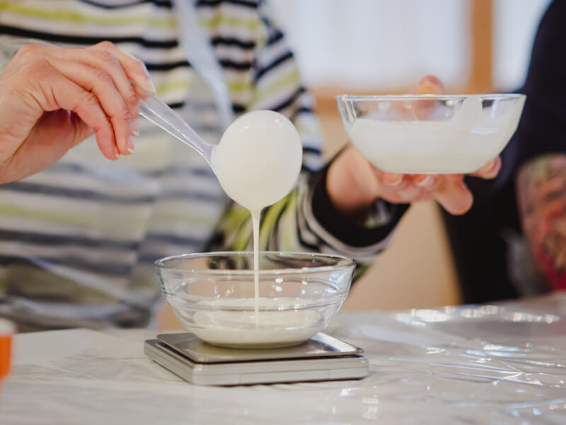 A close up of a person pouring melted white chocolate into a glass bowl
